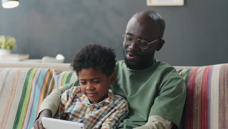 Cheerful-African-American-Boy-Playing-with-Dad-on-Digital-Tablet-at-Home